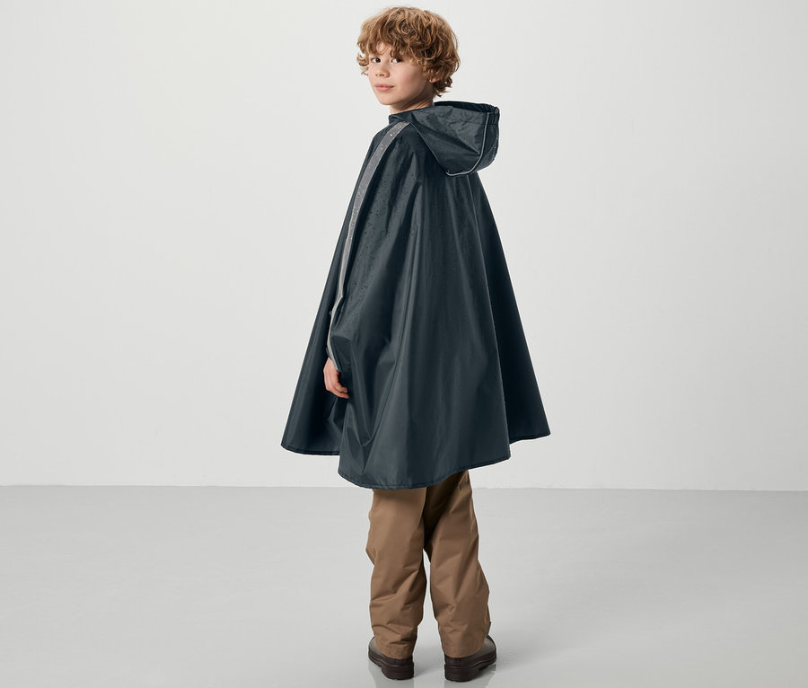 Un garçon regarde par-dessus son épaule et porte un poncho de pluie bleu pour enfants.