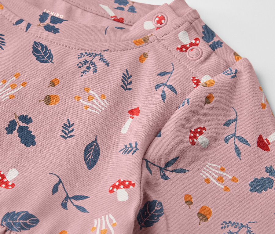 Gros plan sur une robe en jersey rose pour enfants avec un imprimé de feuilles et de champignons.