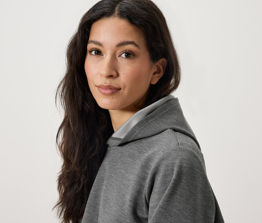 Portrait d'une femme aux longs cheveux foncés portant un sweat à capuche gris.