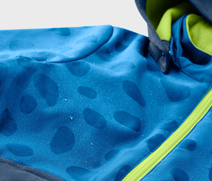 Gros plan sur une veste en softshell bleue pour enfant qui change de couleur quand il pleut, avec une fermeture éclair verte.