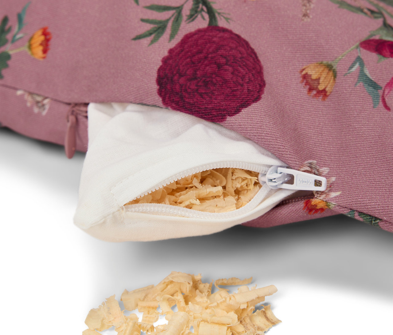Détail d'un coussin violet à motif floral, avec une fermeture éclair blanche ouverte et un rembourrage en copeaux de bois.