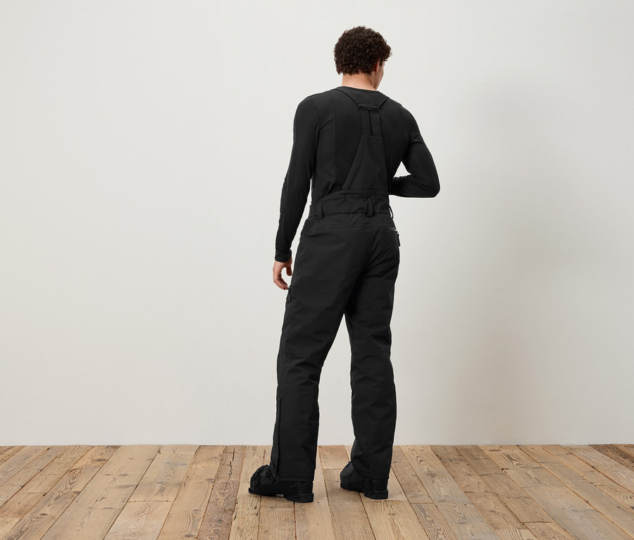 Un homme, vu de dos, porte une salopette noire et un t-shirt noir à manches longues.