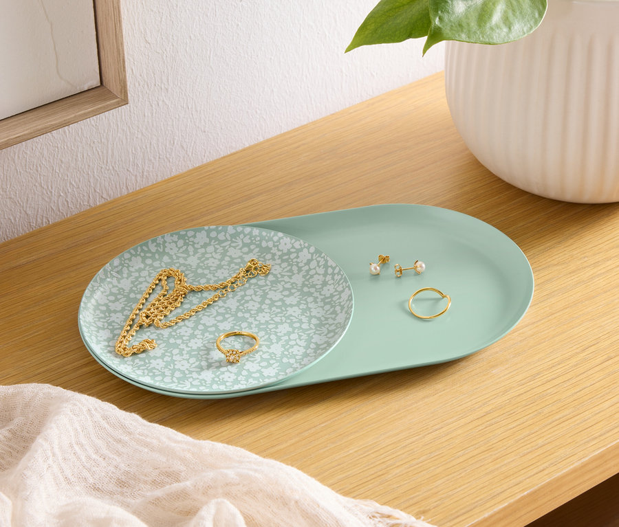 Sur une étagère en bois se trouve un plateau vert avec un collier en or, une bague et des boucles d'oreilles. À côté du plateau se trouve un vase blanc.