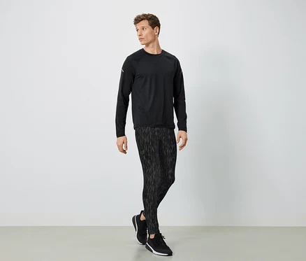 Un homme en vêtements de sport noirs pose sur un fond clair.