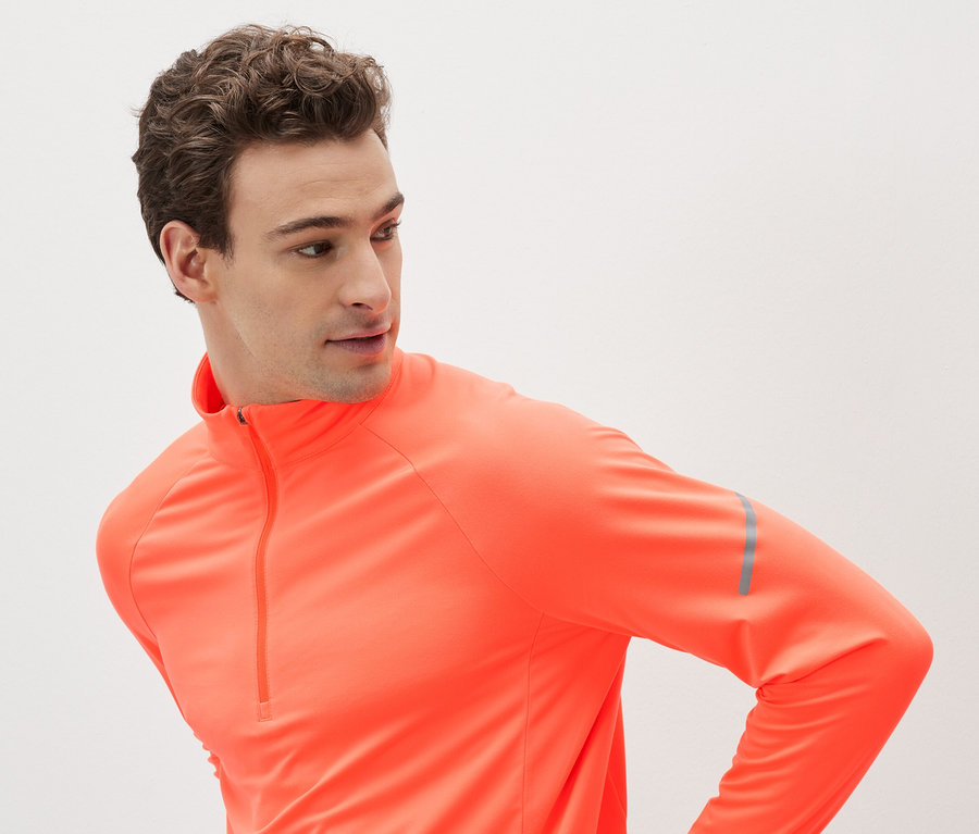 Homme portant un maillot de sport orange à manches longues avec fermeture éclair.