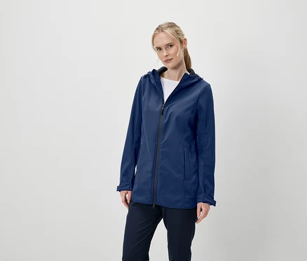 Une femme pose en portant une veste softshell bleu foncé à capuche et un pantalon bleu foncé.