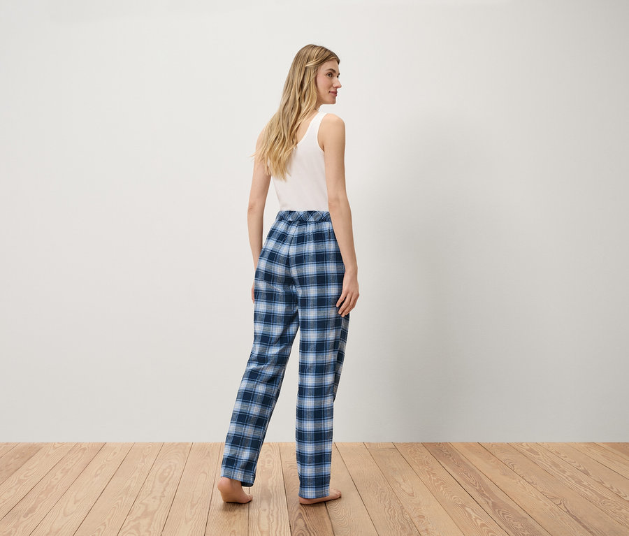 Femme en débardeur blanc et pantalon à carreaux bleus debout sur un plancher en bois.