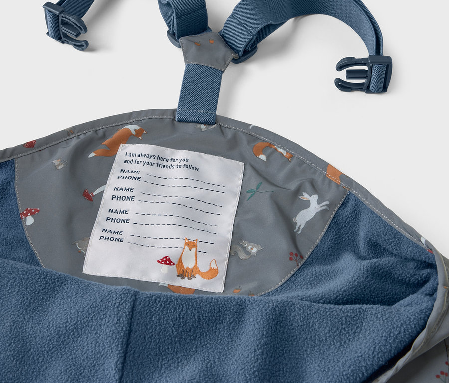 Détail d'un pantalon de pluie thermique pour enfants avec des éléments réfléchissants, intérieur du pantalon imprimé avec des renards, des lièvres et des champignons.