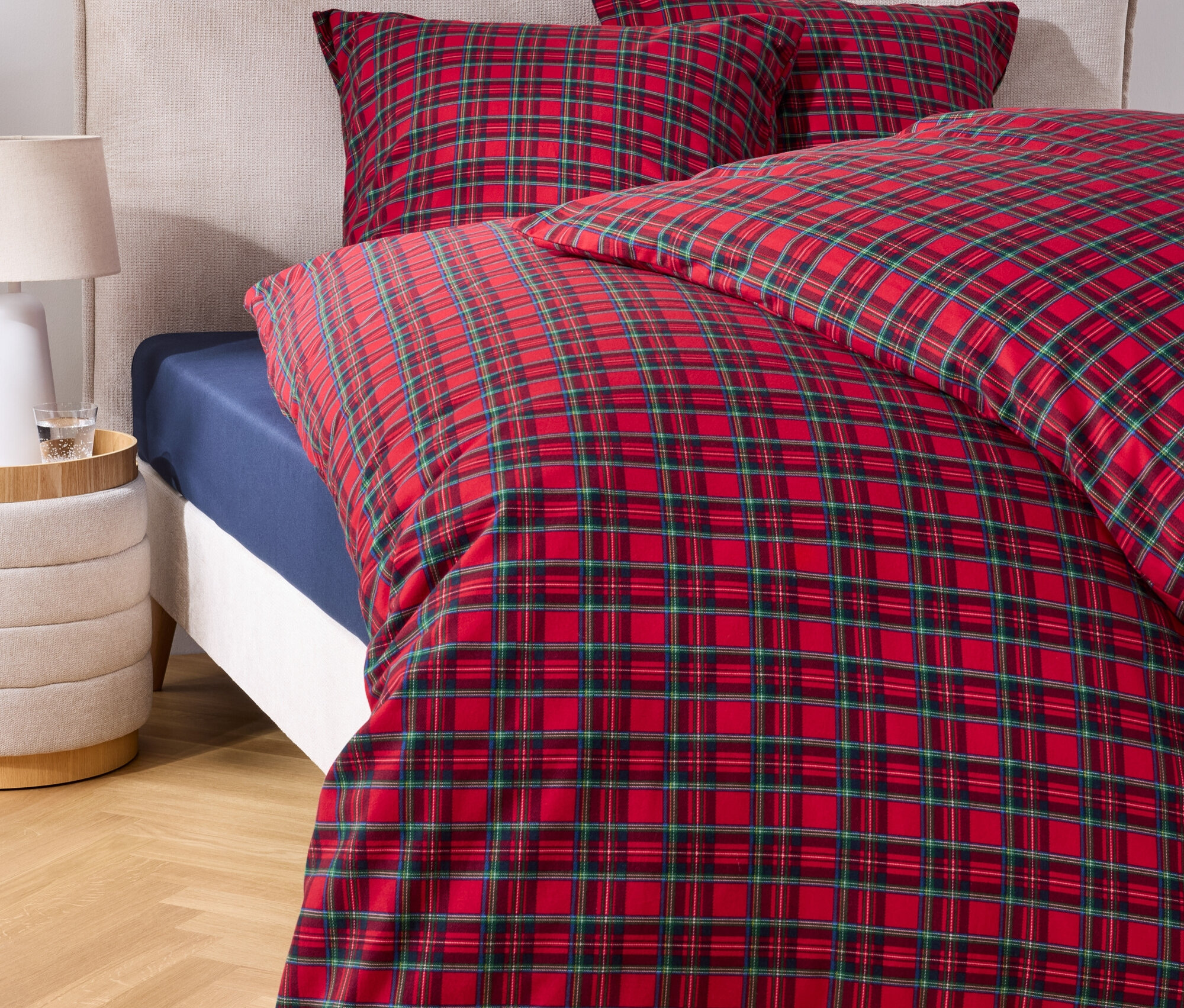 Couvre-lit à carreaux rouge et vert sur un lit avec deux oreillers et une table de chevet.