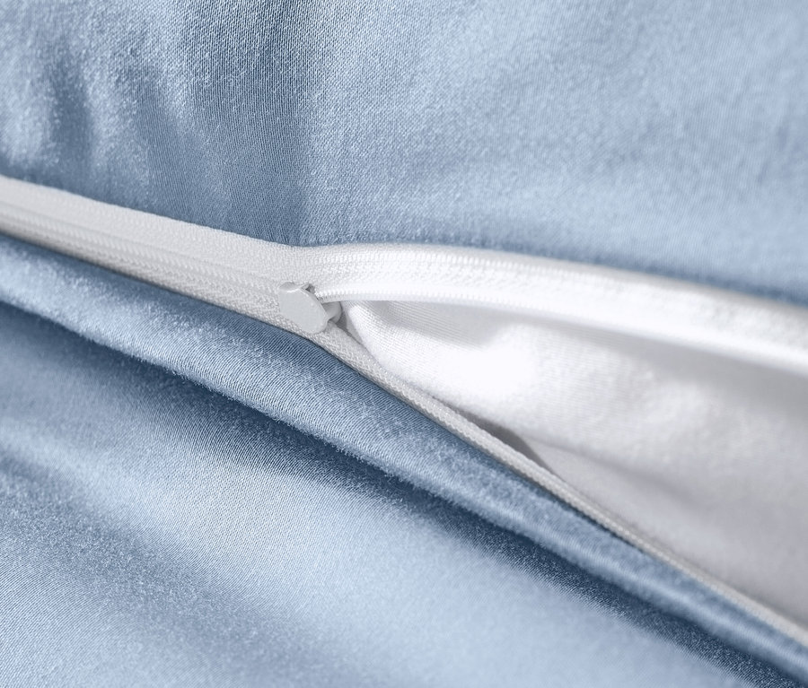 Gros plan sur une parure de lit en satin de coton bleu clair avec une fermeture éclair blanche.