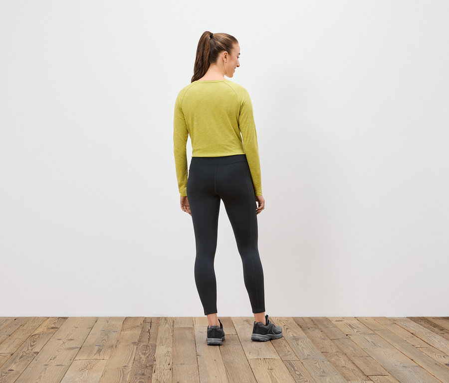 Une femme, dos à la caméra, porte un haut à manches longues vert olive, un legging noir et des baskets.