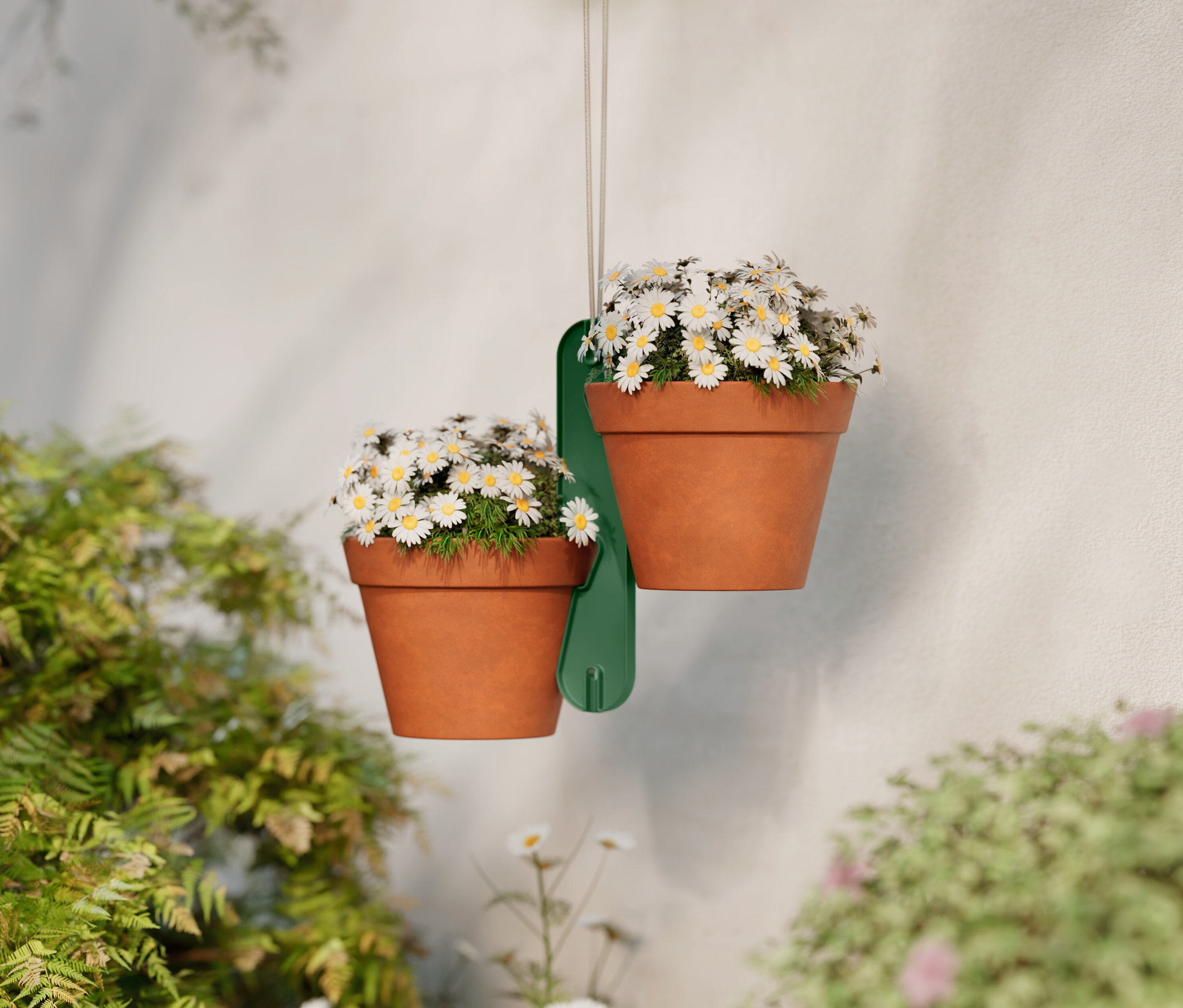 Deux pots de fleurs en terre cuite avec des marguerites suspendus à un support vert devant un mur blanc.