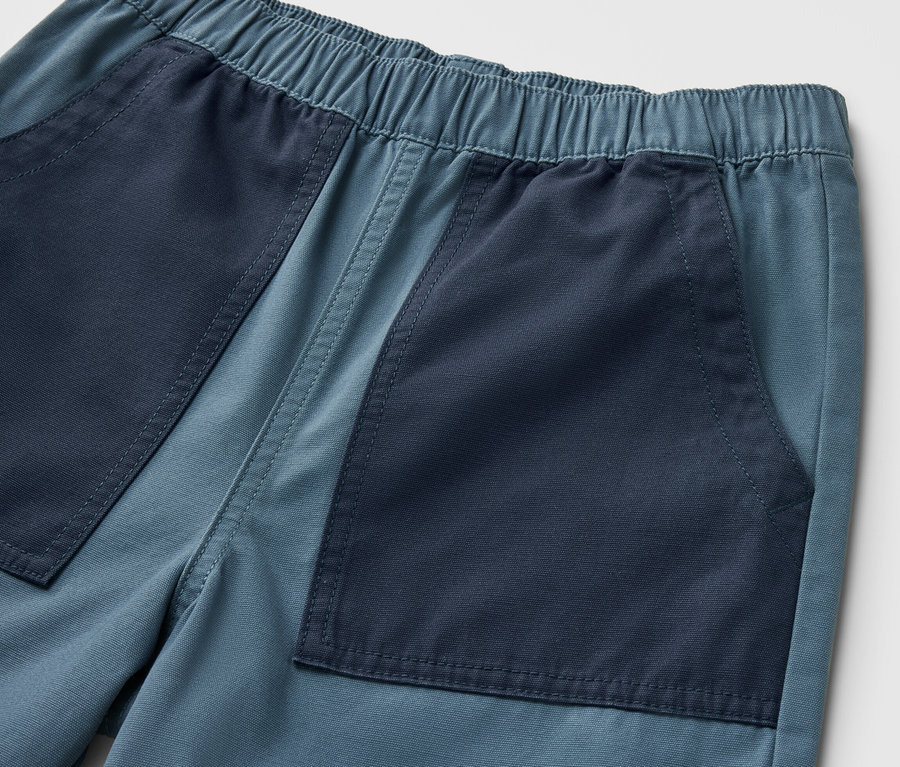 Gros plan sur un bermuda pour enfant avec des poches bleu foncé sur un fond bleu clair.