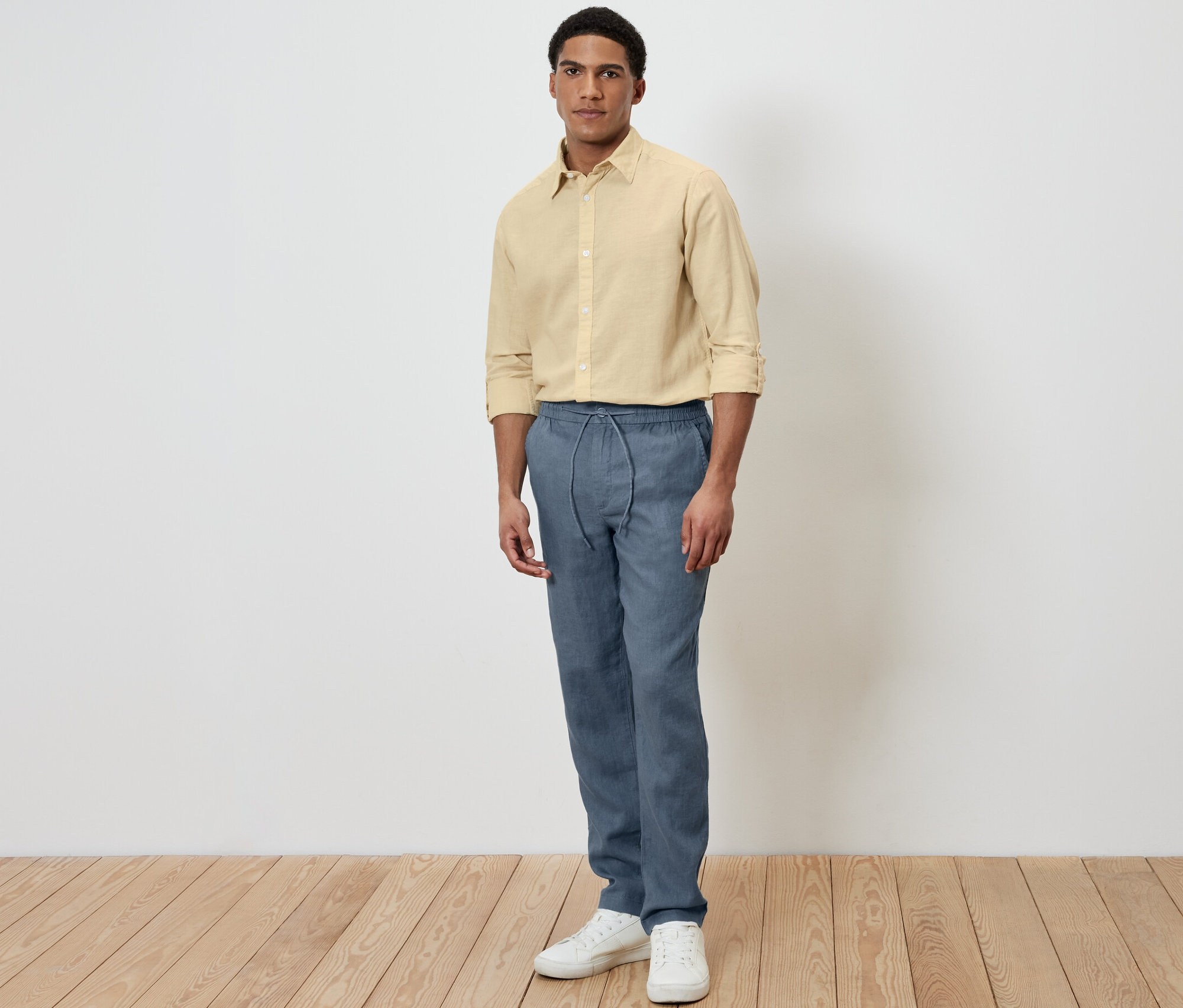 Un homme debout portant un pantalon chino en lin bleu et une chemise jaune.