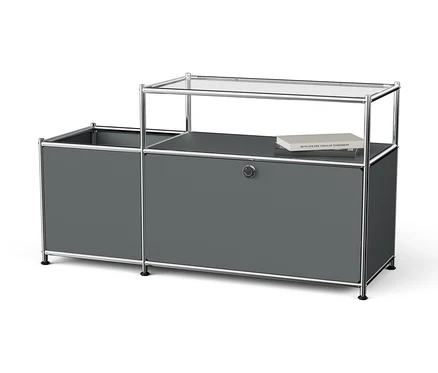 Système de rangement gris avec cadre chromé et plateau en verre sur lequel repose un livre.