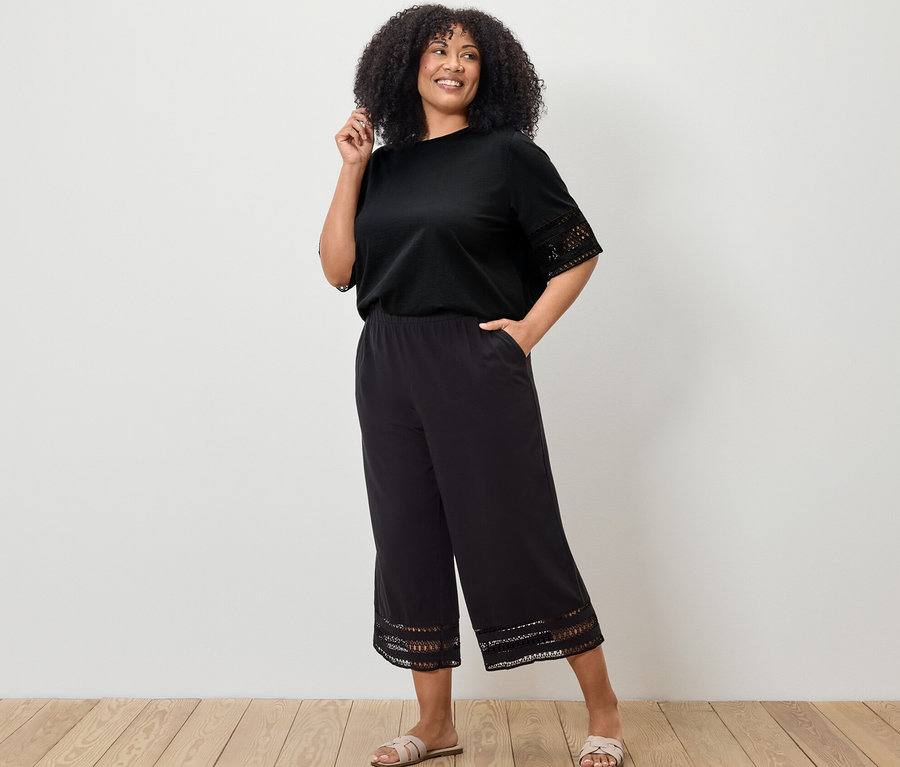 Femme posant dans un t-shirt noir à broderie et un bas large noir à broderie.