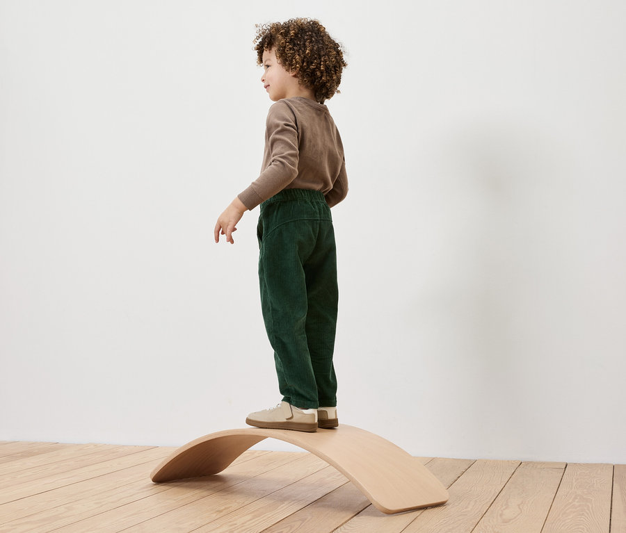 Un garçon aux cheveux bouclés se tient sur une planche d'équilibre en bois.