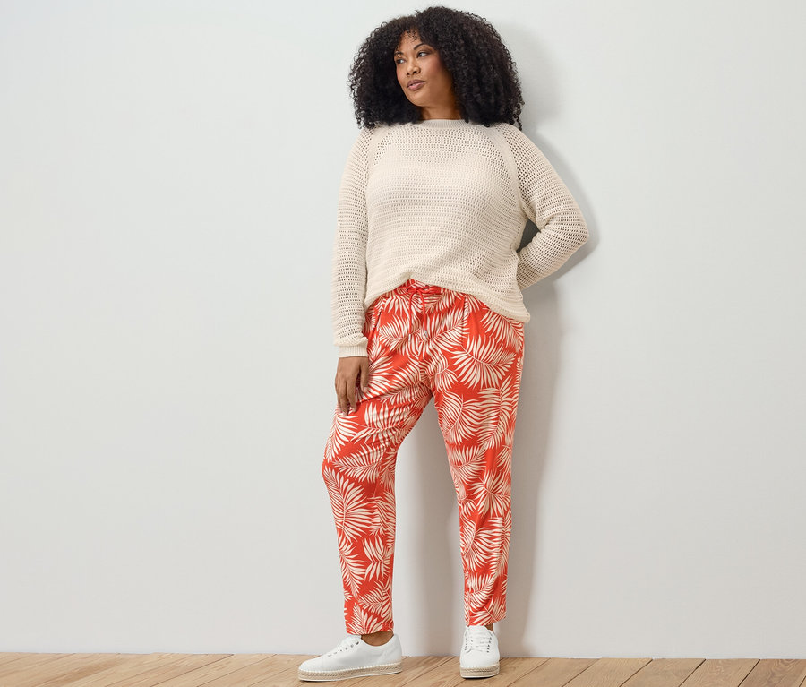 Une femme pose portant un pull en maille pointelle et un pantalon en jersey imprimé.