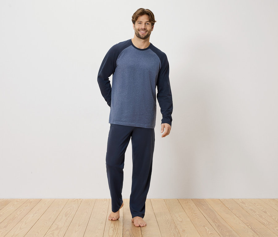 Un homme se tient pieds nus sur un plancher en bois, portant un pyjama bleu marine.