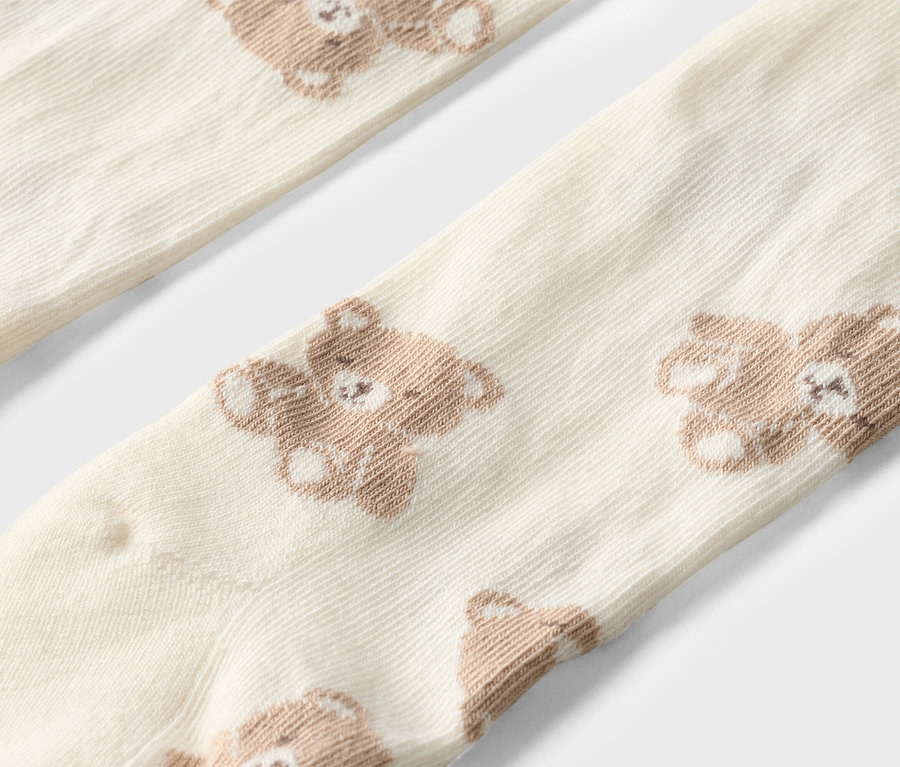 Gros plan de deux chaussettes crème avec des ours en peluche marron.