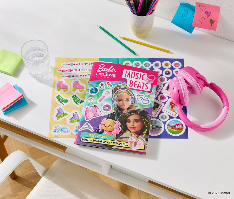 Sur un bureau, un casque rose est posé à côté d'un livre de coloriage Barbie, d'une planche d'autocollants, de stylos, de notes et d'un verre d'eau.