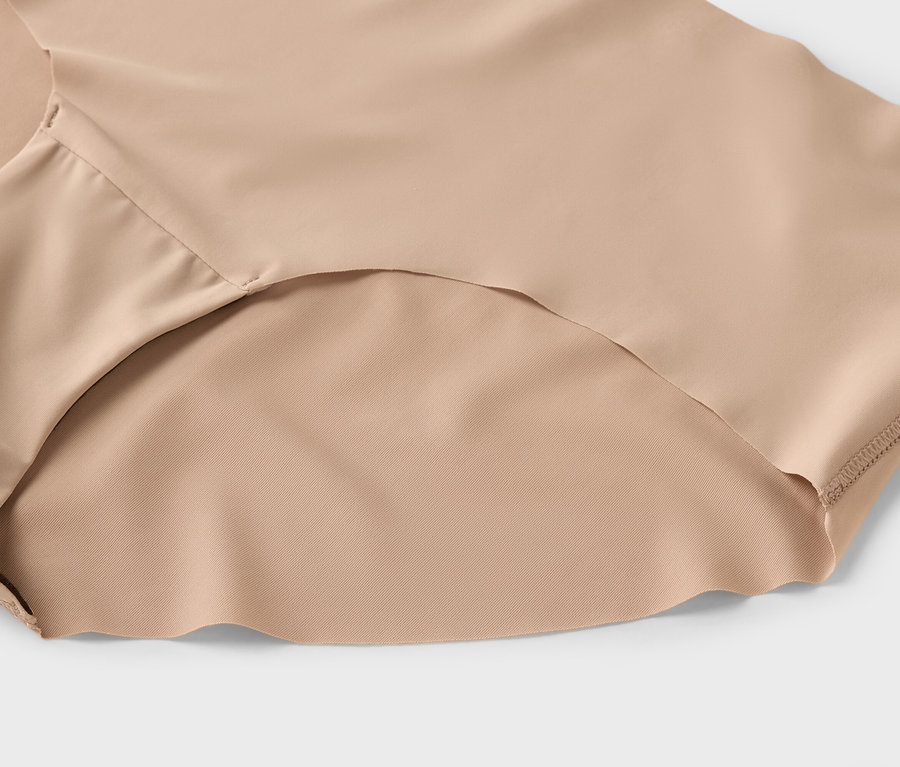 Gros plan de sous-vêtements beiges pour femmes sur un fond gris clair.