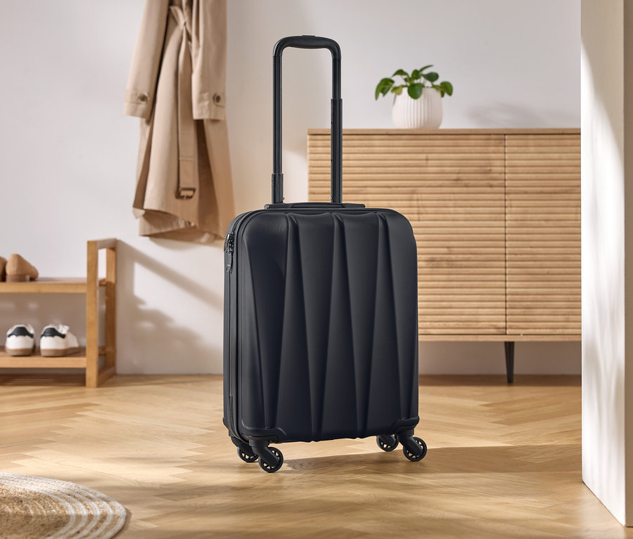 Valise noire à roulettes avec poignée extensible posée sur un parquet en bois clair.