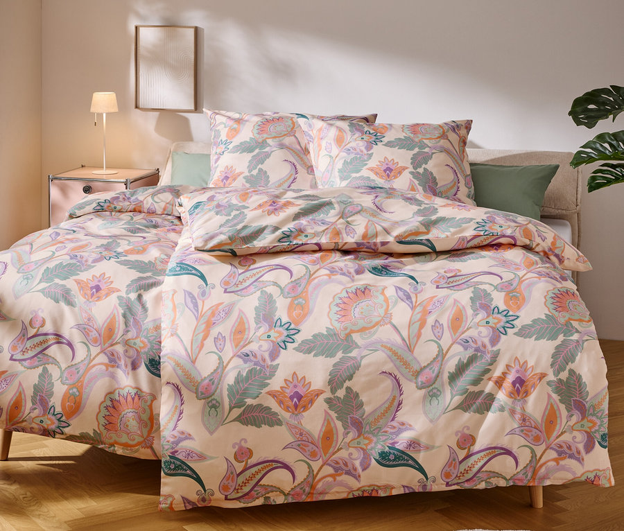 Un lit avec une literie claire à motifs floraux se trouve dans une chambre.