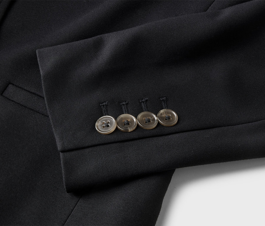 Gros plan sur une veste de costume noire avec quatre boutons marron clair sur la manche et une poche.