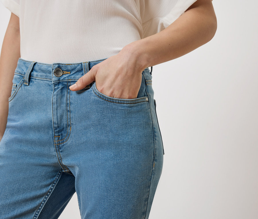 Femme avec la main dans la poche d'un jean bleu clair, portant un haut blanc.