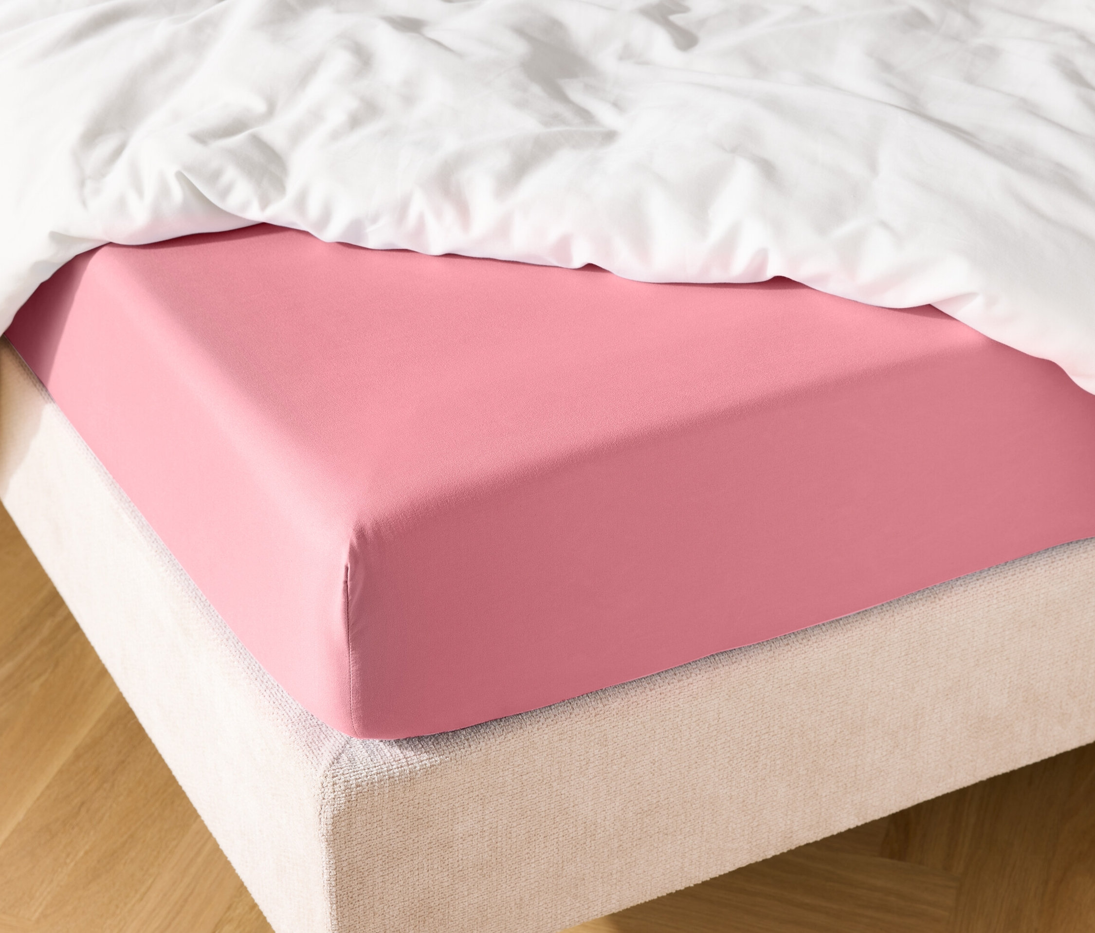 Gros plan d'un lit avec un drap-housse rose et une couette blanche.