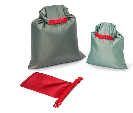 Trois sacs de rangement de différentes tailles et couleurs (gris, bleu-vert et rouge) sont posés sur un fond blanc. Chaque sac est muni d'une fermeture rouge.