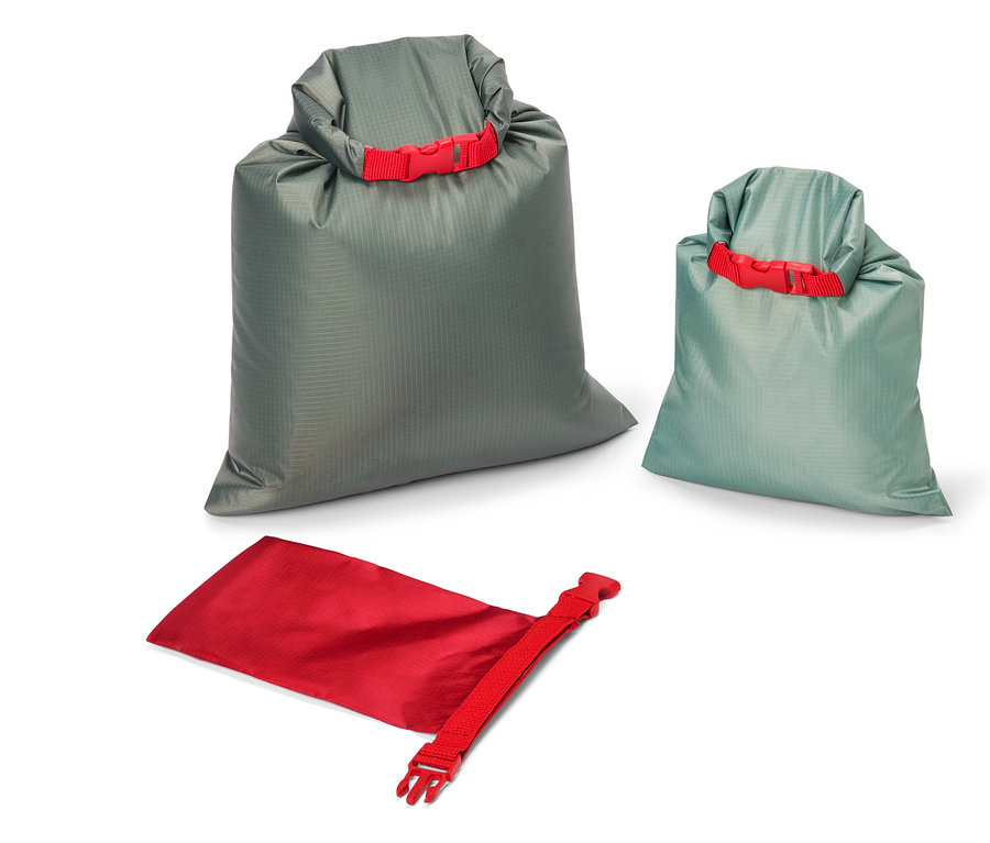 Trois sacs de rangement de différentes tailles et couleurs (gris, bleu-vert et rouge) sont posés sur un fond blanc. Chaque sac est muni d'une fermeture rouge.