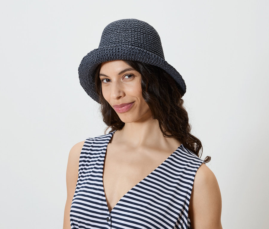 Une femme aux cheveux ondulés foncés porte un chapeau en crochet bleu marine et un débardeur rayé.