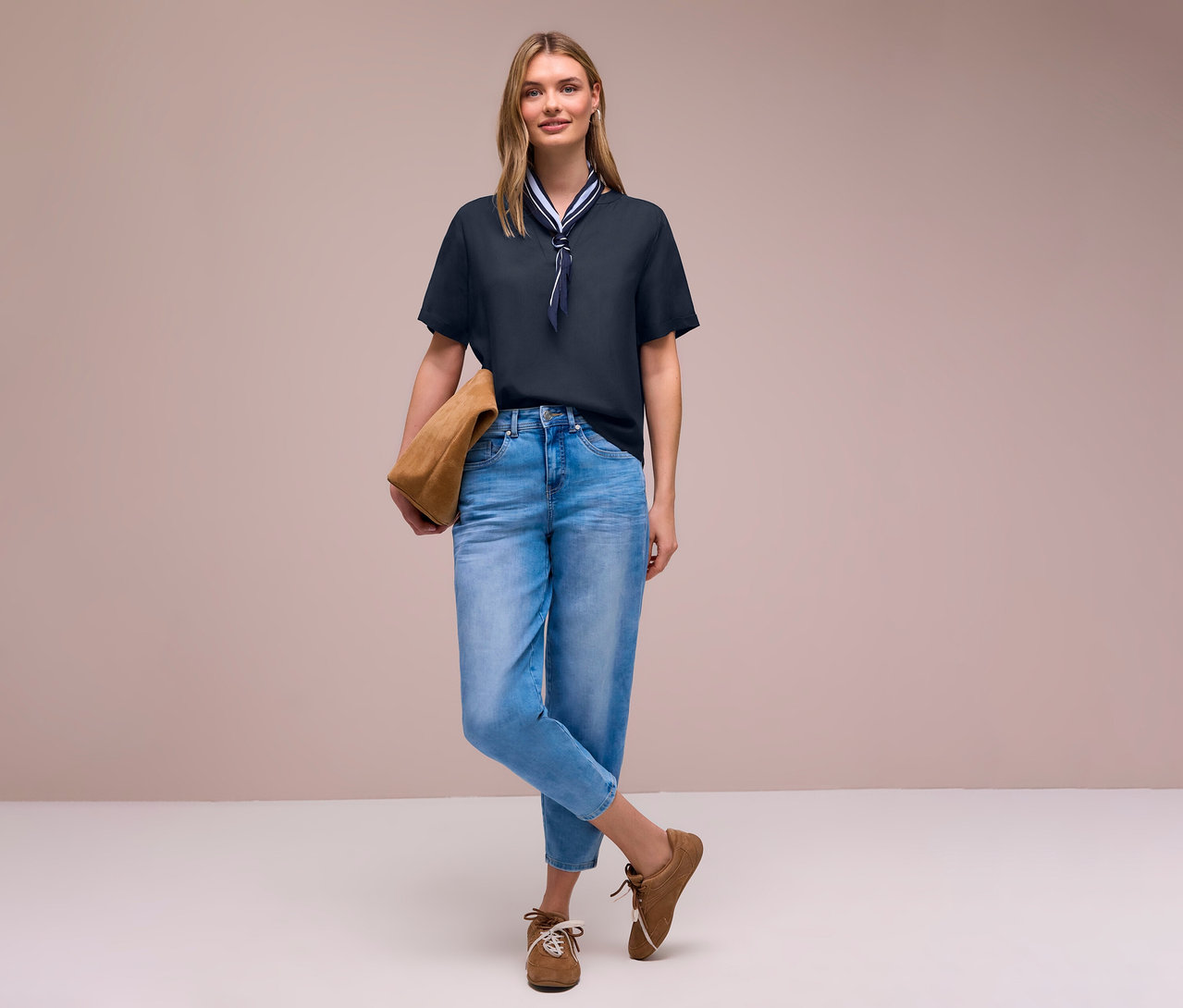 Une femme en jean et chaussures marron avec un sac, porte une blouse en maille Street One avec un foulard.