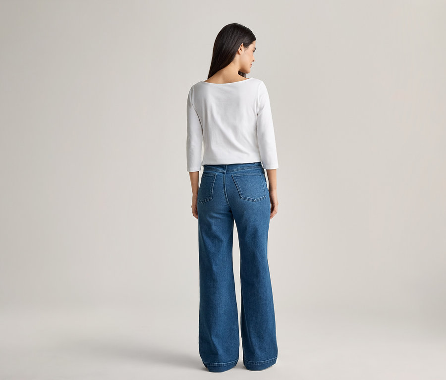 Vue de dos d'une femme aux cheveux foncés portant un haut blanc à manches longues et un jean bleu ample.