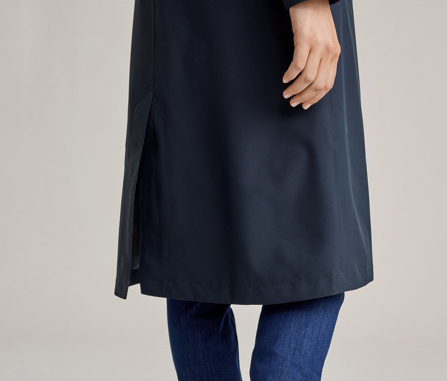 Gros plan d'une personne portant un jean et un long manteau bleu marine avec une fente.
