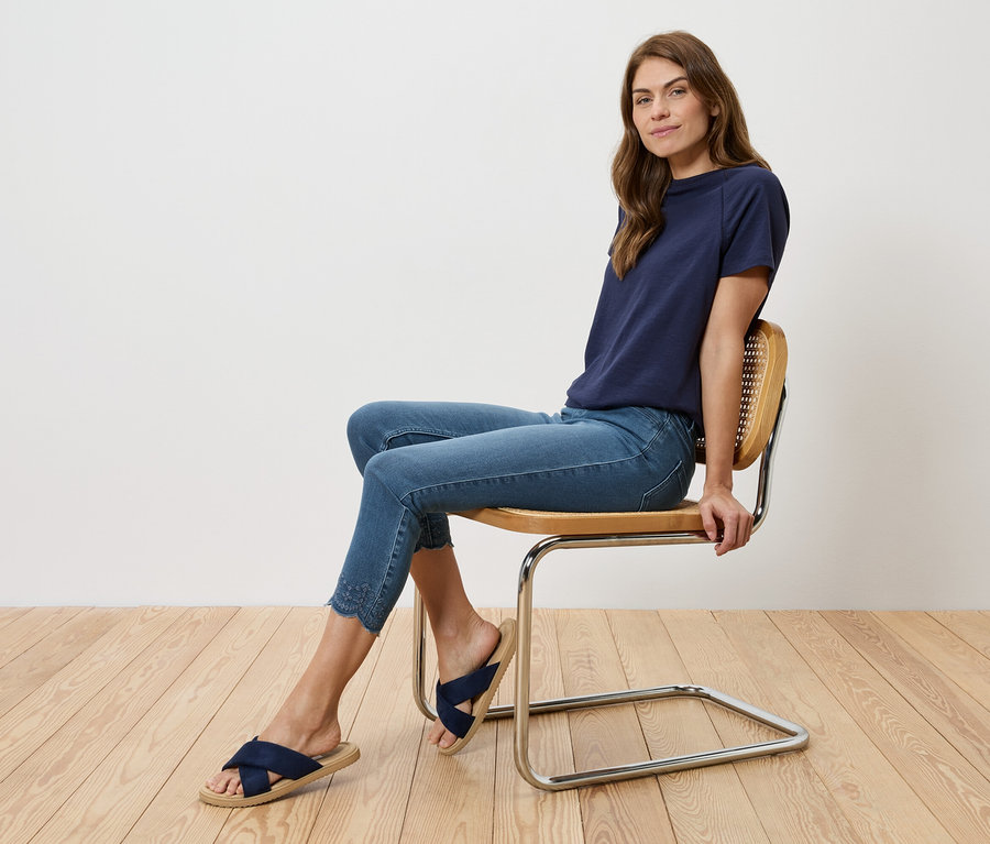 Femme assise sur une chaise portant un t-shirt bleu marine, un jean bleu et des sandales bleu marine.