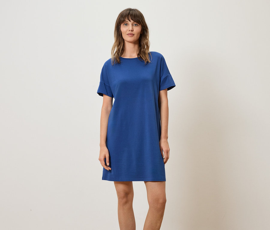 Femme portant une robe t-shirt bleue sur un fond neutre.