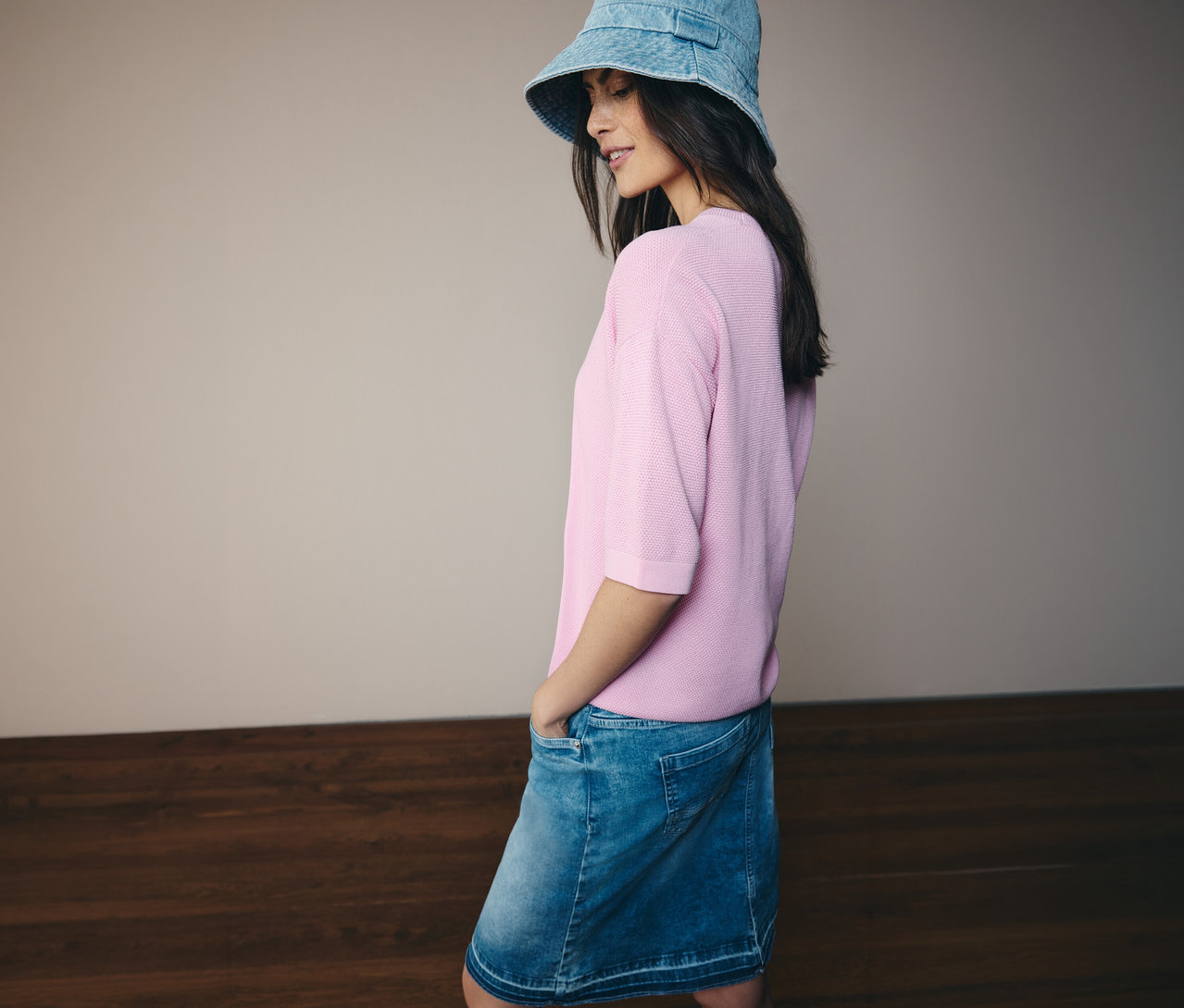 Femme portant un chapeau en jean, un pull à manches courtes rose CECIL et une jupe en jean CECIL. Elle a les mains dans les poches.
