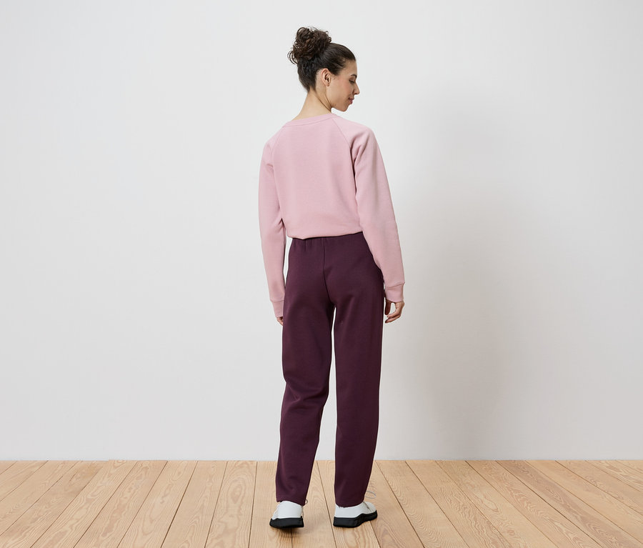 Vue arrière d'une femme avec un chignon portant un sweat-shirt rose et un pantalon bordeaux.