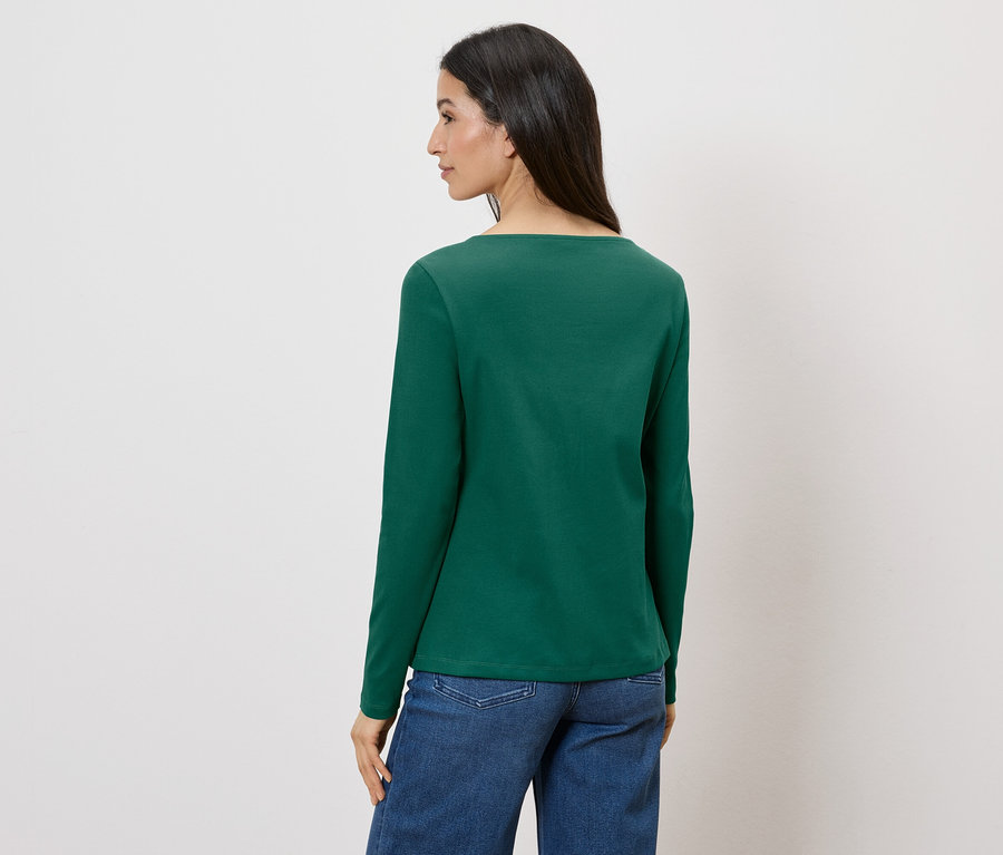Une femme, vue de dos, porte un t-shirt vert à manches longues et un jean sur un fond blanc.