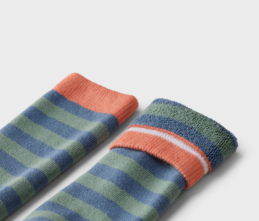 Gros plan de deux chaussettes rayées vertes et bleues avec des bords-côtes orange.