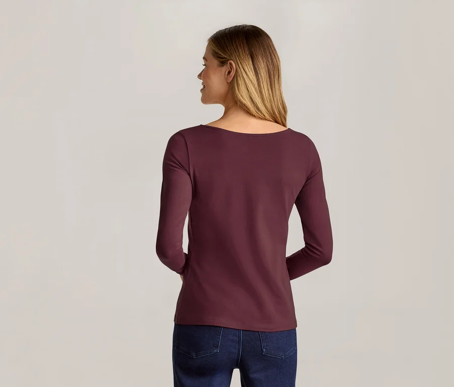 Femme vue de dos, portant un t-shirt à manches longues bordeaux et un jean sur un fond gris clair.