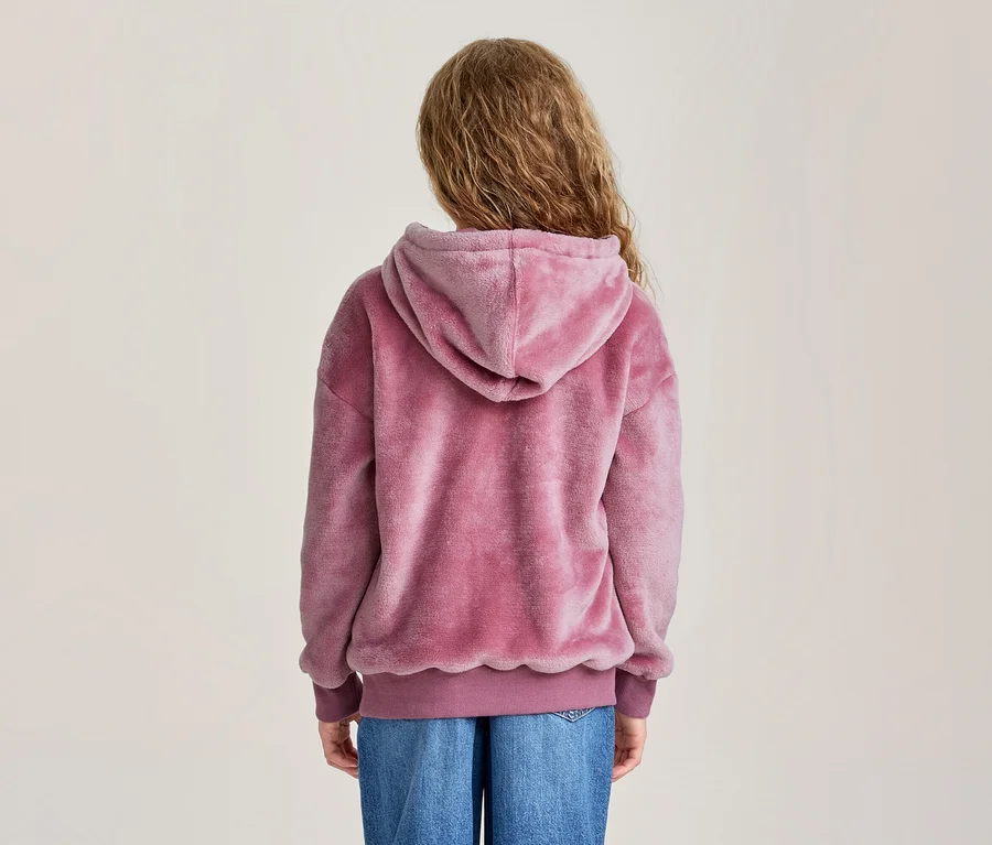 Personne vue de dos, portant un sweat à capuche rose duveteux et un jean bleu.