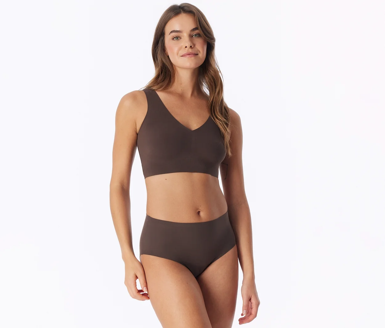 Femme aux longs cheveux bruns portant un soutien-gorge marron et une culotte taille haute assortie, debout devant un fond blanc.