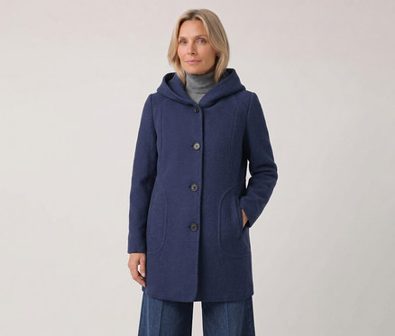 Femme portant un manteau bleu à capuche sur un col roulé gris, la main gauche dans la poche du manteau, regardant devant elle.