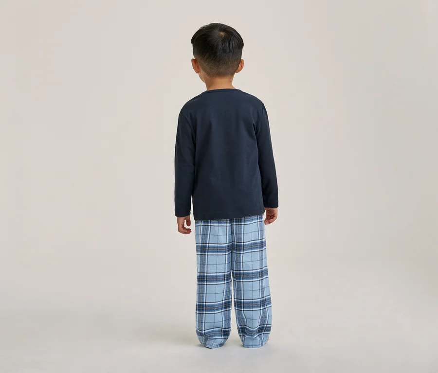 Un enfant vu de dos, portant un t-shirt à manches longues bleu foncé et un pantalon de pyjama à carreaux bleus.