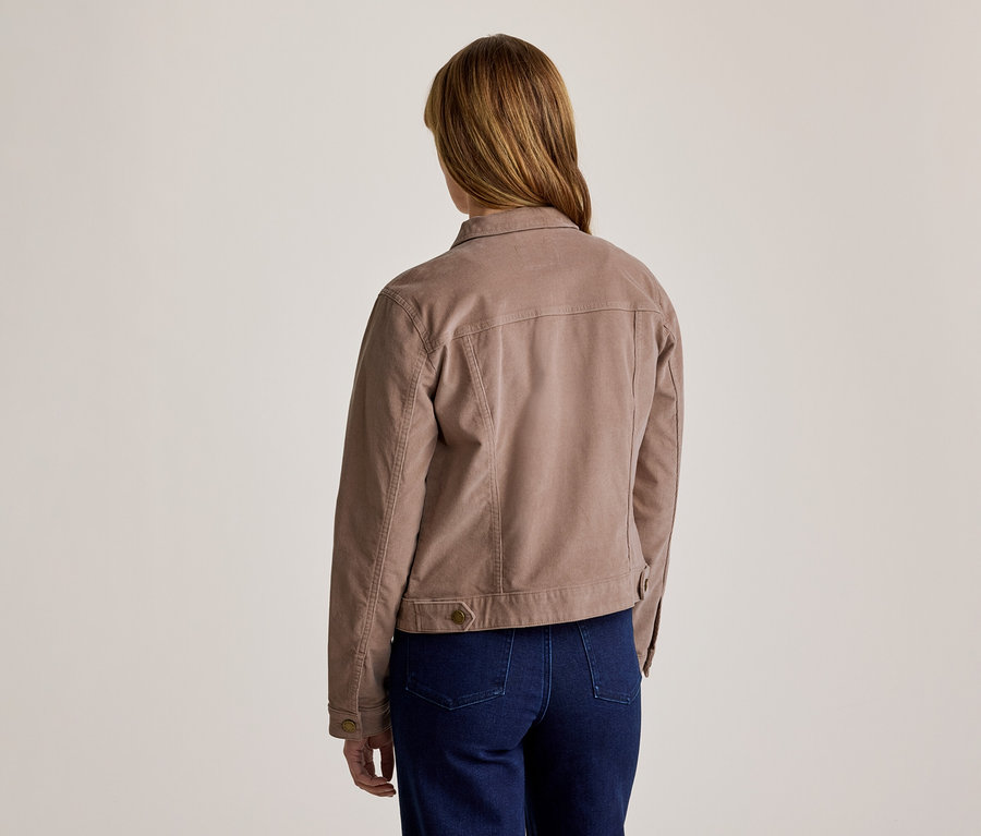 Femme vue de dos, portant une veste marron clair à col avec des coutures visibles et un jean bleu foncé.