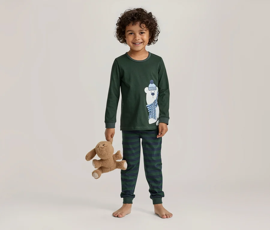 Garçon souriant aux cheveux bouclés portant un pyjama vert foncé avec un ours polaire et un pantalon rayé, tenant une peluche marron.
